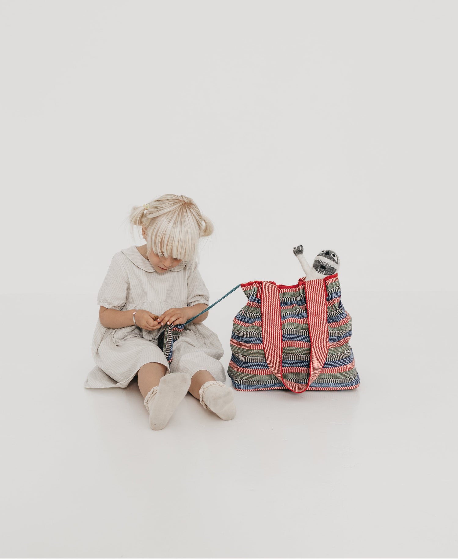 Child sitting on a white floor with Nepali hand-women colorful striped bag and knitting materials.
